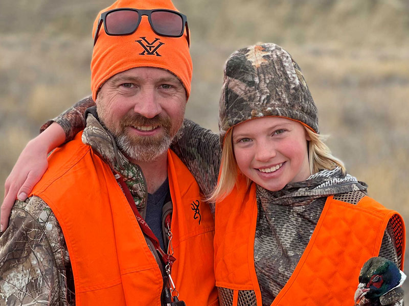 Father and daughter smiling, wearing blaze orange clothing