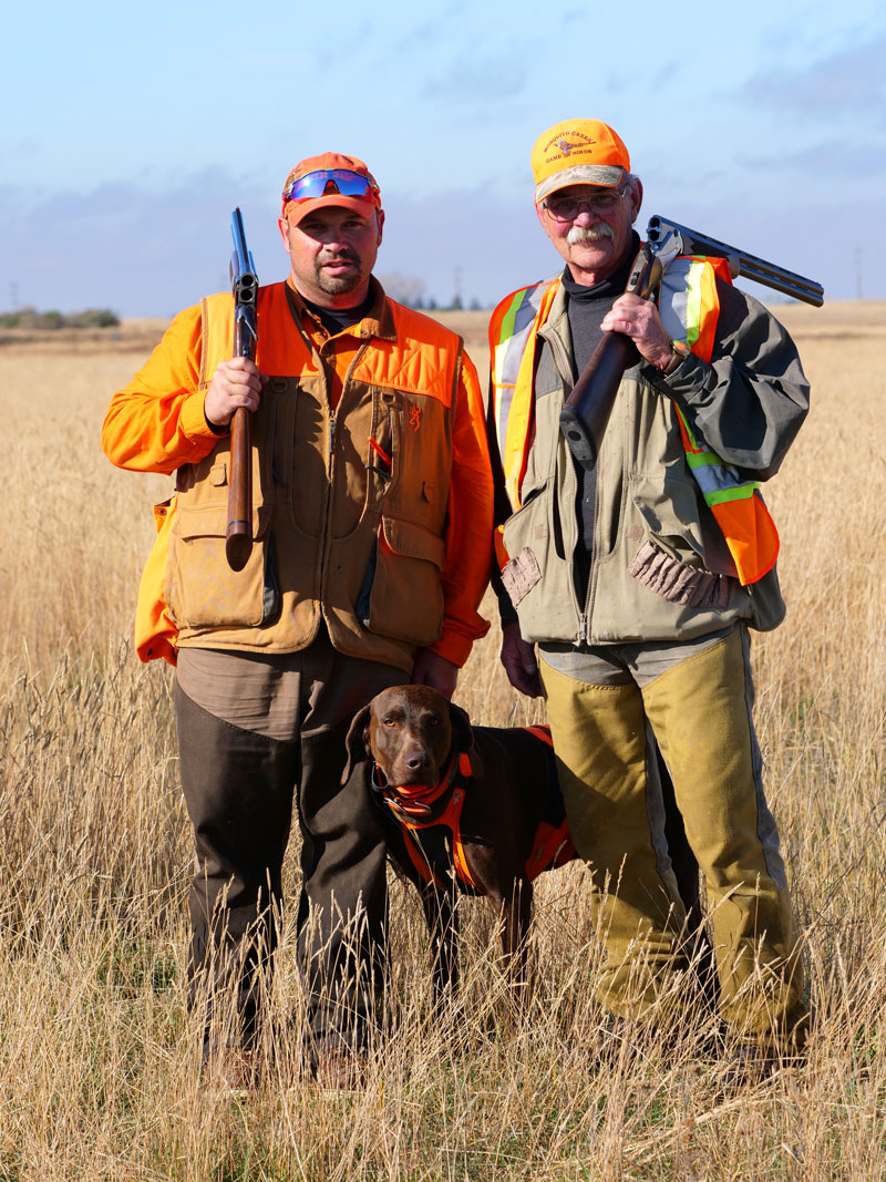 2 hunters standing in a field with a dog